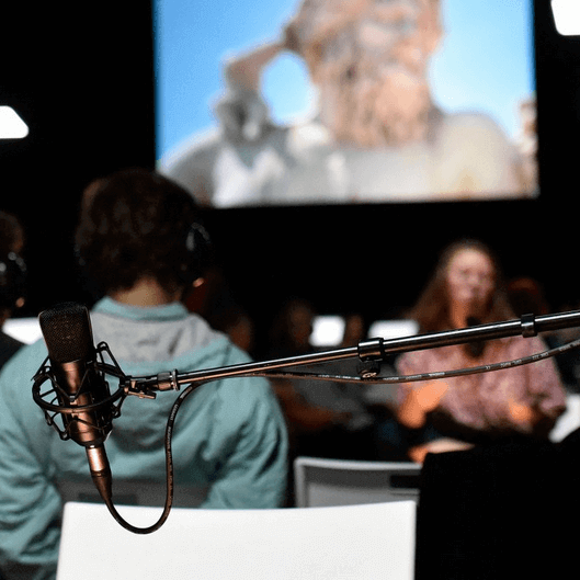 Image du spectacle Reconstitution ; un micro en premier plan et des spectateurs flous